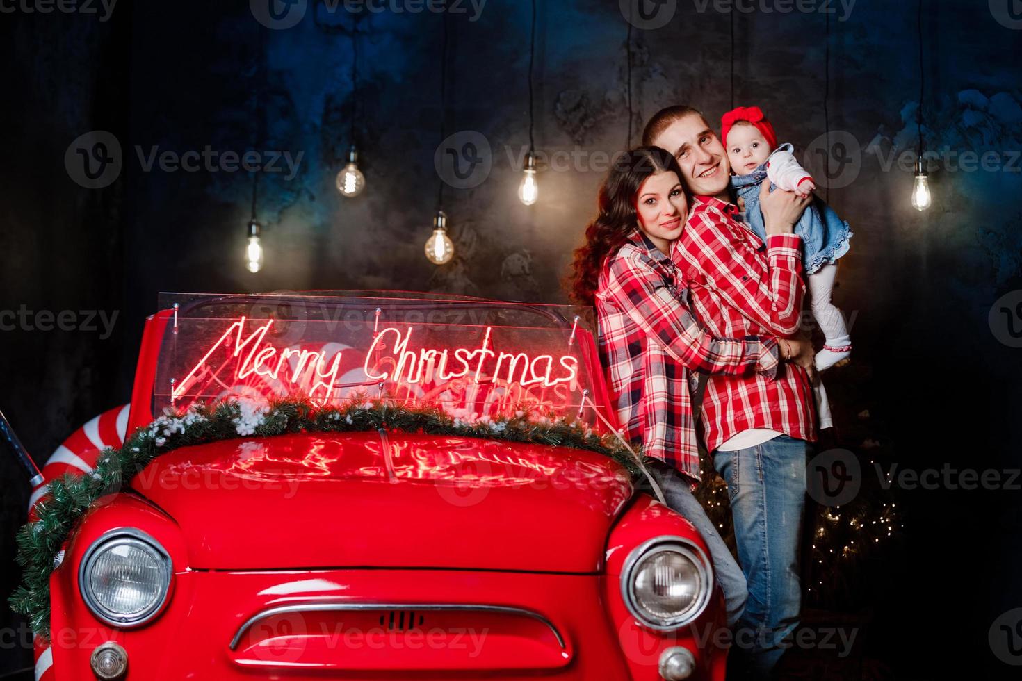 jovens pais lindos segurando sua filha bonita em seus braços se divertindo perto de carro retrô em estúdio. olhar de família de natal. cenário de ano novo. foto