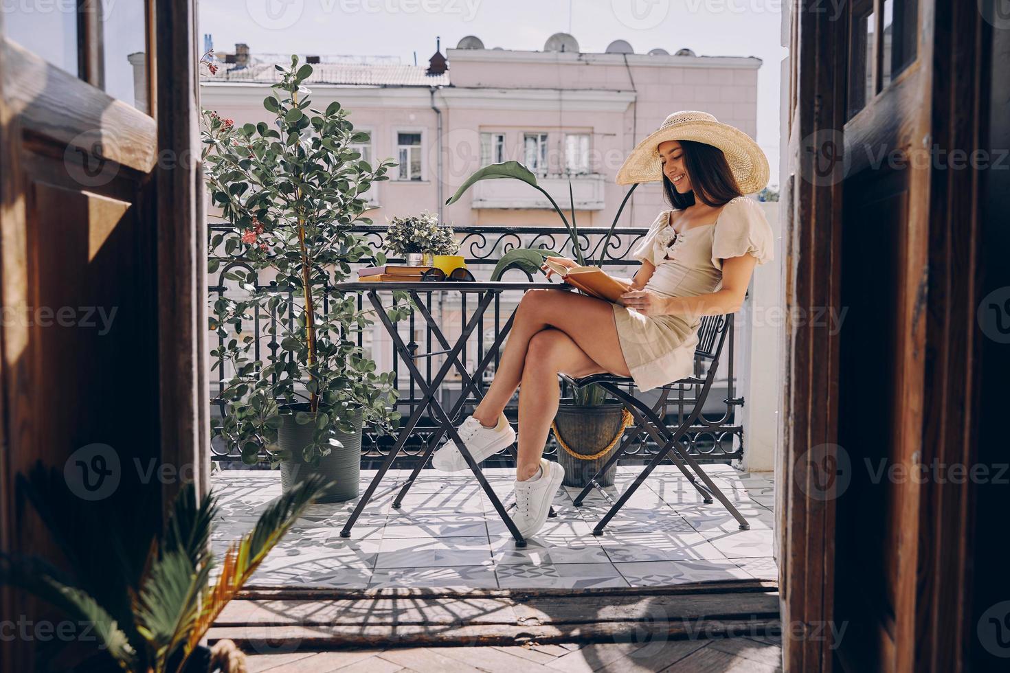 mulher jovem feliz no livro de leitura de chapéu elegante enquanto relaxa na varanda foto