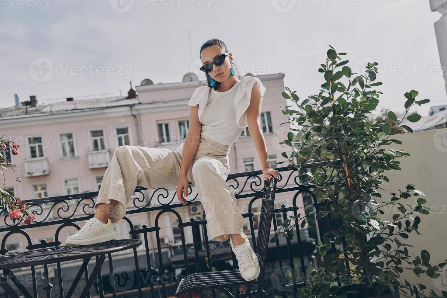 moda jovem em óculos olhando para a câmera enquanto está sentado na varanda foto