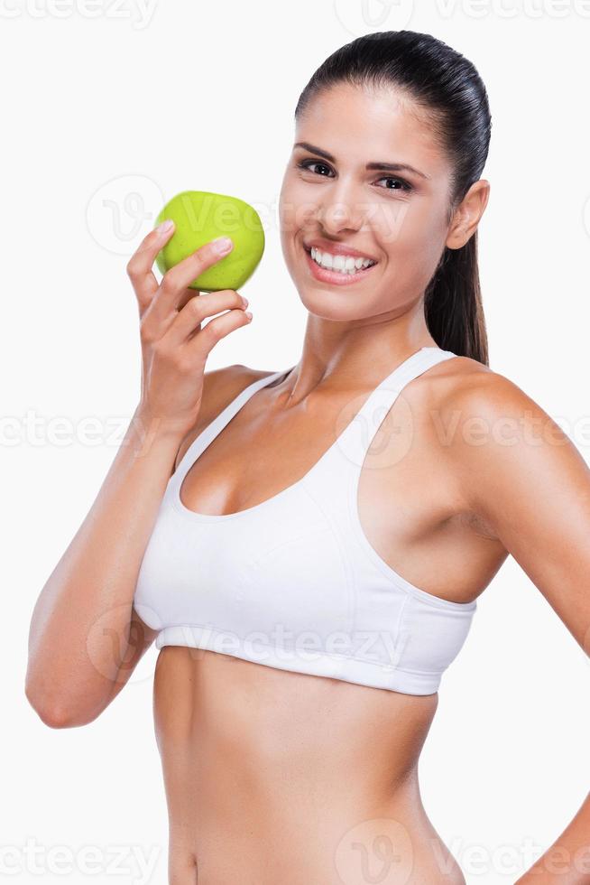Junte-se a uma jovem atraente de estilo de vida saudável em sutiã branco e calcinha segurando maçã verde e sorrindo em pé isolado no branco foto
