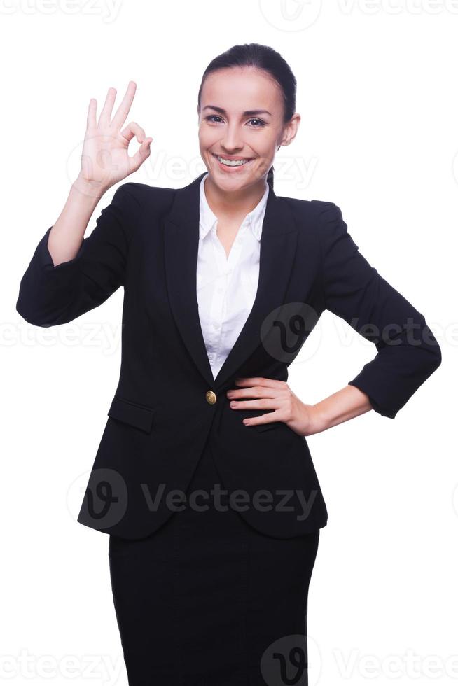 está tudo bem jovem feliz em traje formal, gesticulando sinal de ok e sorrindo em pé isolado no branco foto