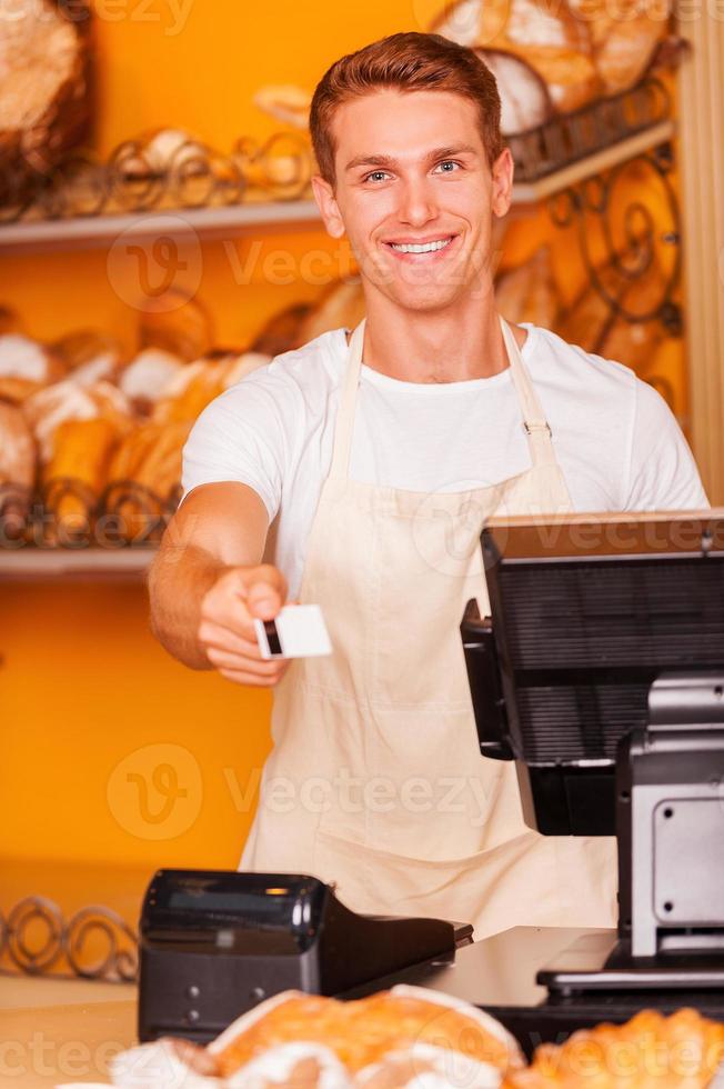 aqui está o seu cartão bonito caixa masculino esticando o cartão de plástico e sorrindo em pé na padaria foto