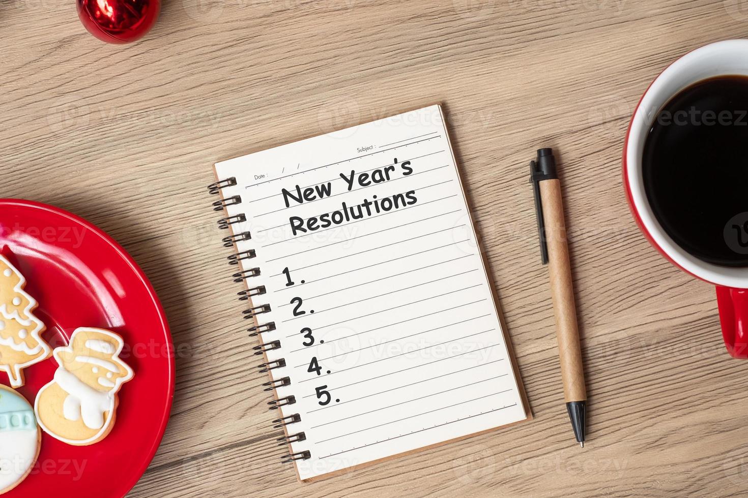 resolução de ano novo com notebook, xícara de café preto, biscoitos de natal e caneta na mesa de madeira. natal, feliz ano novo, objetivos, lista de tarefas, estratégia e conceito de plano foto