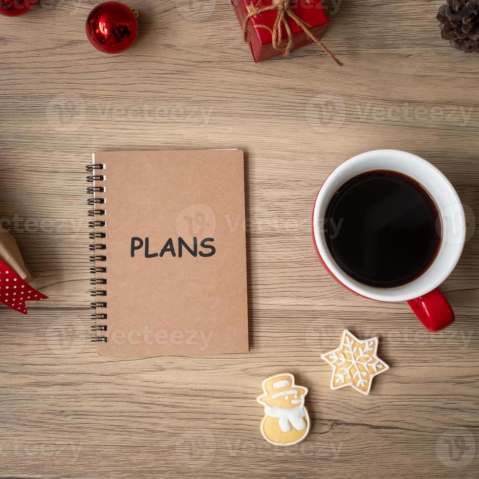 caderno, xícara de café preto, biscoitos de natal e caneta na mesa de madeira, vista superior e espaço de cópia. natal, feliz ano novo, objetivos, resolução, lista de tarefas, estratégia e conceito de plano foto