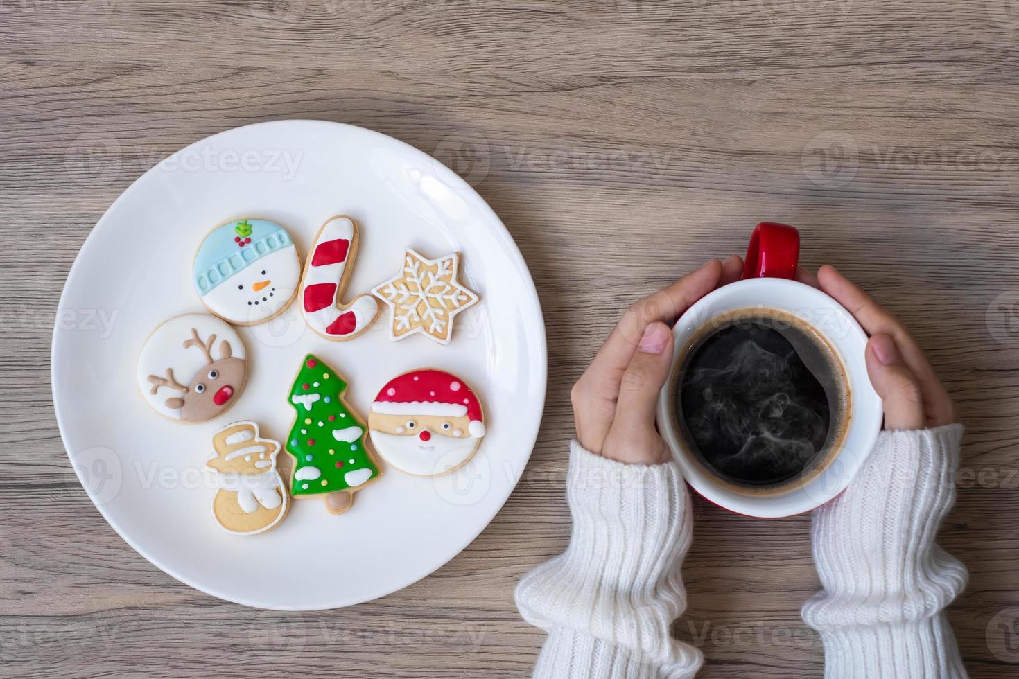 feliz natal com mão de mulher segurando a xícara de café e biscoito caseiro na mesa. véspera de natal, festa, feriado e feliz ano novo conceito foto