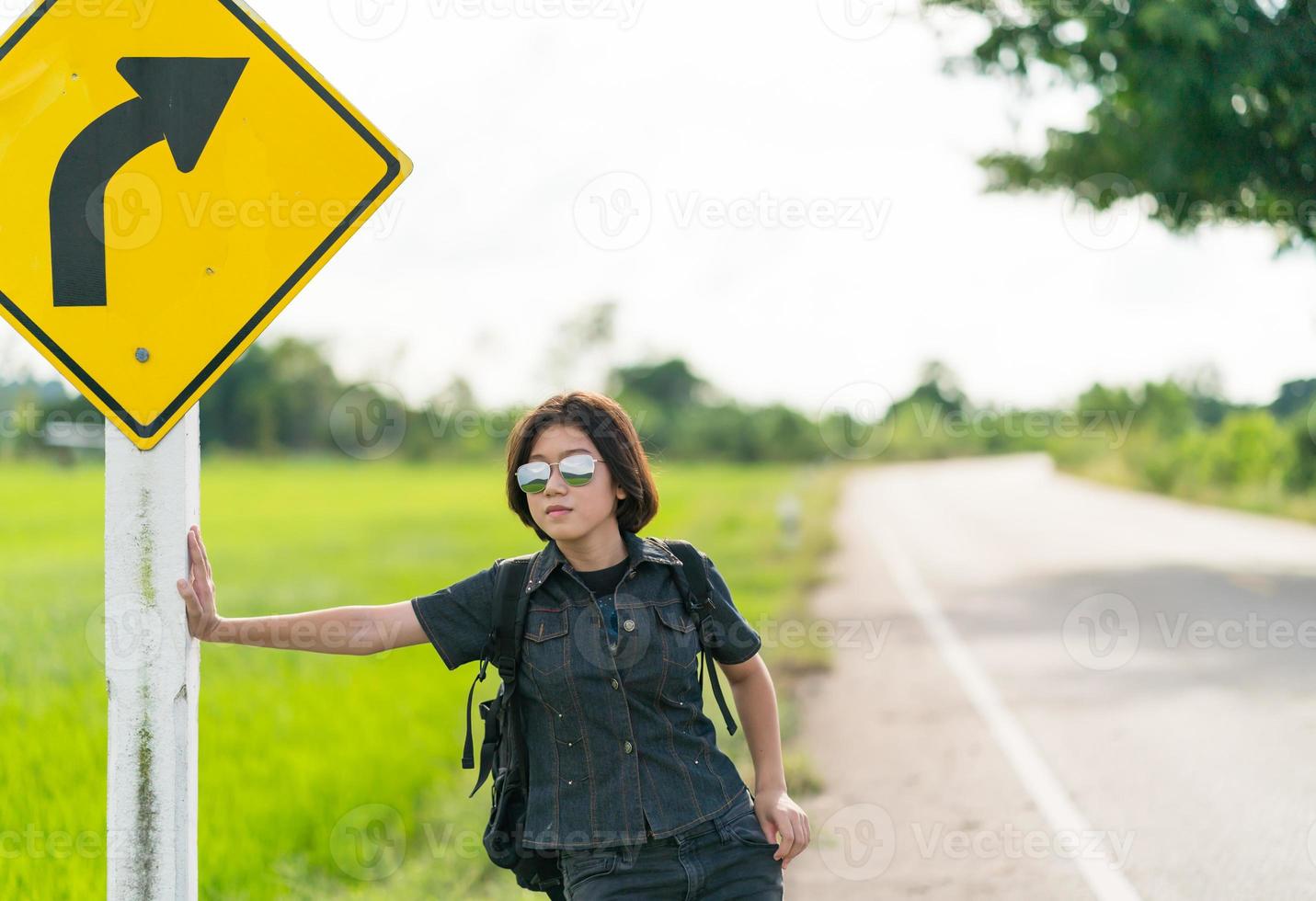 mulher fica com mochila pedindo carona ao longo de uma estrada foto