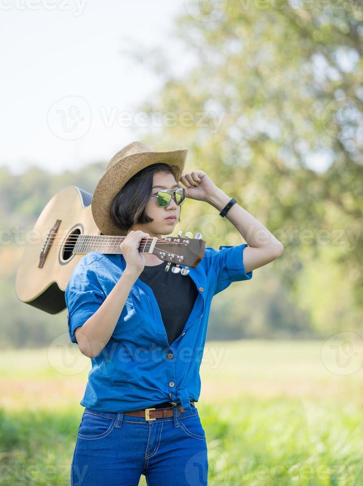 mulher usa chapéu e carrega seu violão no campo de grama foto