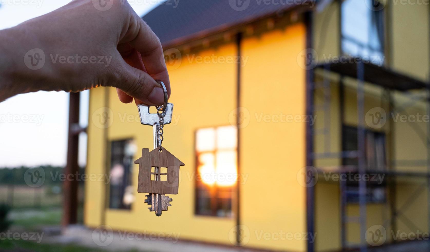 uma mão com as chaves de uma nova casa no fundo de uma casa inacabada. construir, projetar, mudar para uma nova casa, hipotecar, alugar e comprar imóveis. para abrir a porta. espaço de cópia foto