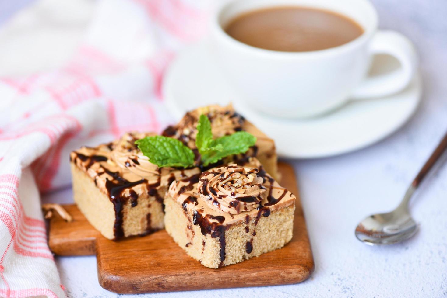 bolo de café deliciosa sobremesa servida na mesa - fatia de bolo de chocolate no fundo da placa de madeira com folha de hortelã e xícara de café no café da manhã foto