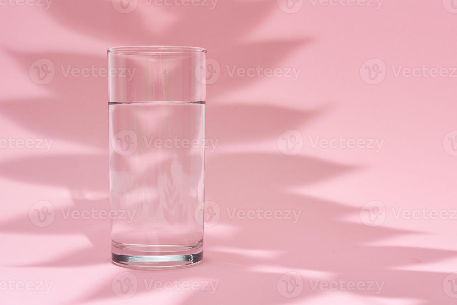 copo de água e sombra de folha em um fundo rosa foto