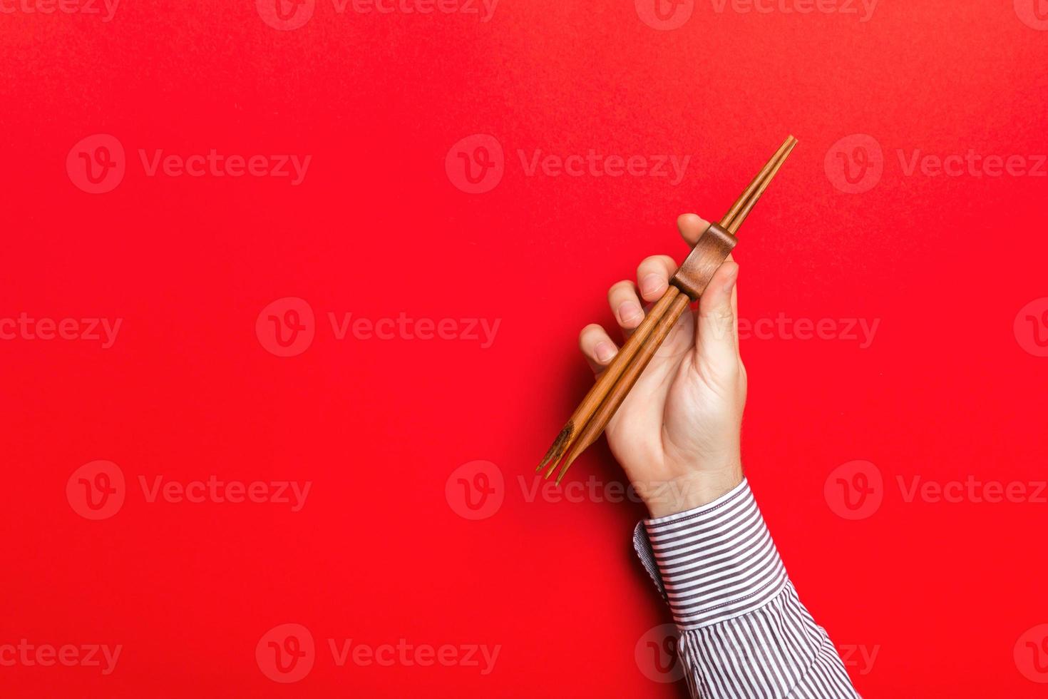 imagem recortada da mão masculina segurando os pauzinhos sobre fundo vermelho. conceito de comida asiática com espaço de cópia foto