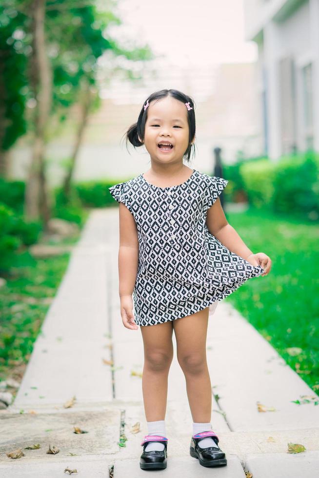 menina asiática feliz em um vestido em pé na calçada do parque foto