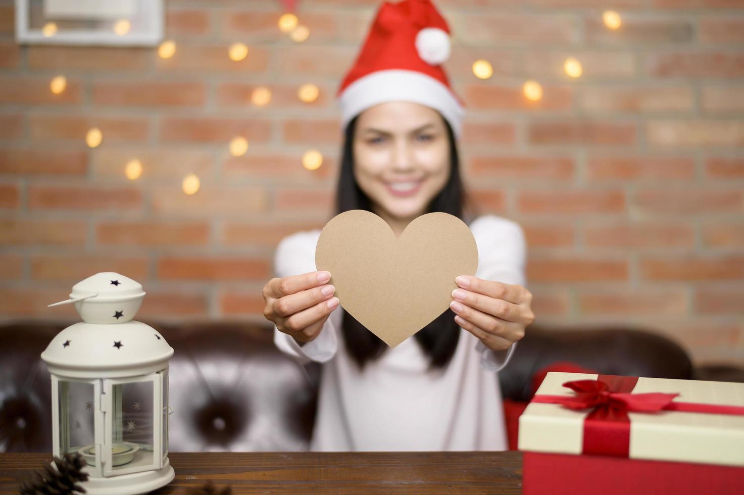 jovem sorridente com chapéu de Papai Noel vermelho mostrando um coração foto