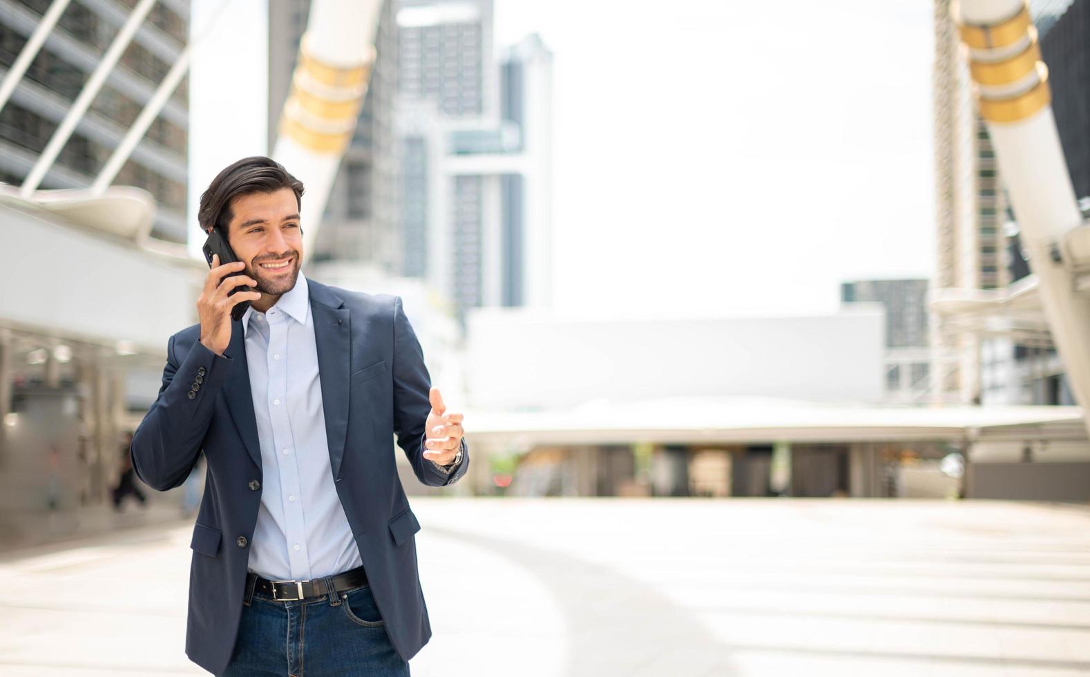 o empresário falando com telefone inteligente em seu caminho. sentindo-se feliz e relaxante, jovem empresário casual vestindo paletó. foto