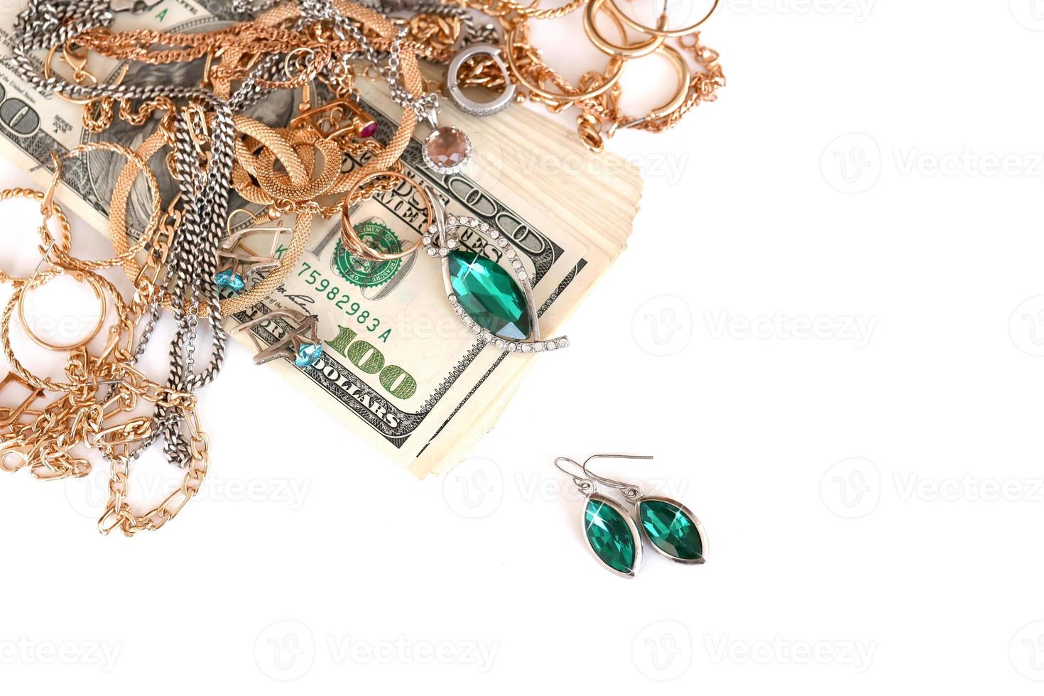 muitos anéis, brincos e colares caros de ouro e prata com grande quantidade de notas de dólar em fundo branco. loja de penhores ou joalheria foto