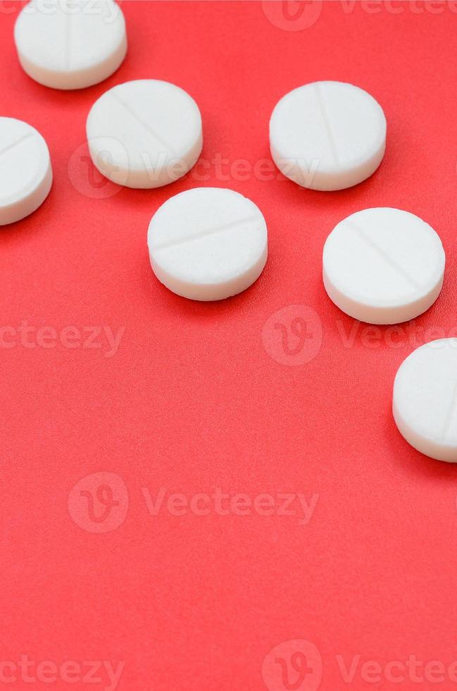 alguns comprimidos brancos repousam sobre uma superfície de fundo vermelho brilhante. imagem de fundo em tópicos médicos e farmacêuticos foto