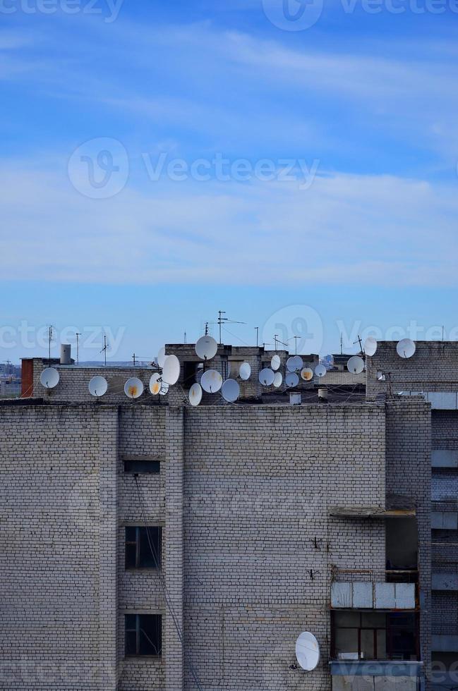 muitas antenas de televisão por satélite no telhado sob um céu azul foto