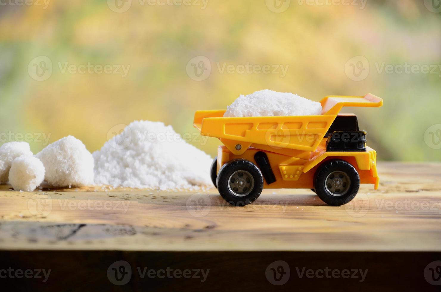 um pequeno caminhão de brinquedo amarelo é carregado com uma pedra de sal branco ao lado de uma pilha de sal. um carro em uma superfície de madeira num contexto de floresta de outono. extração e transporte de sal foto