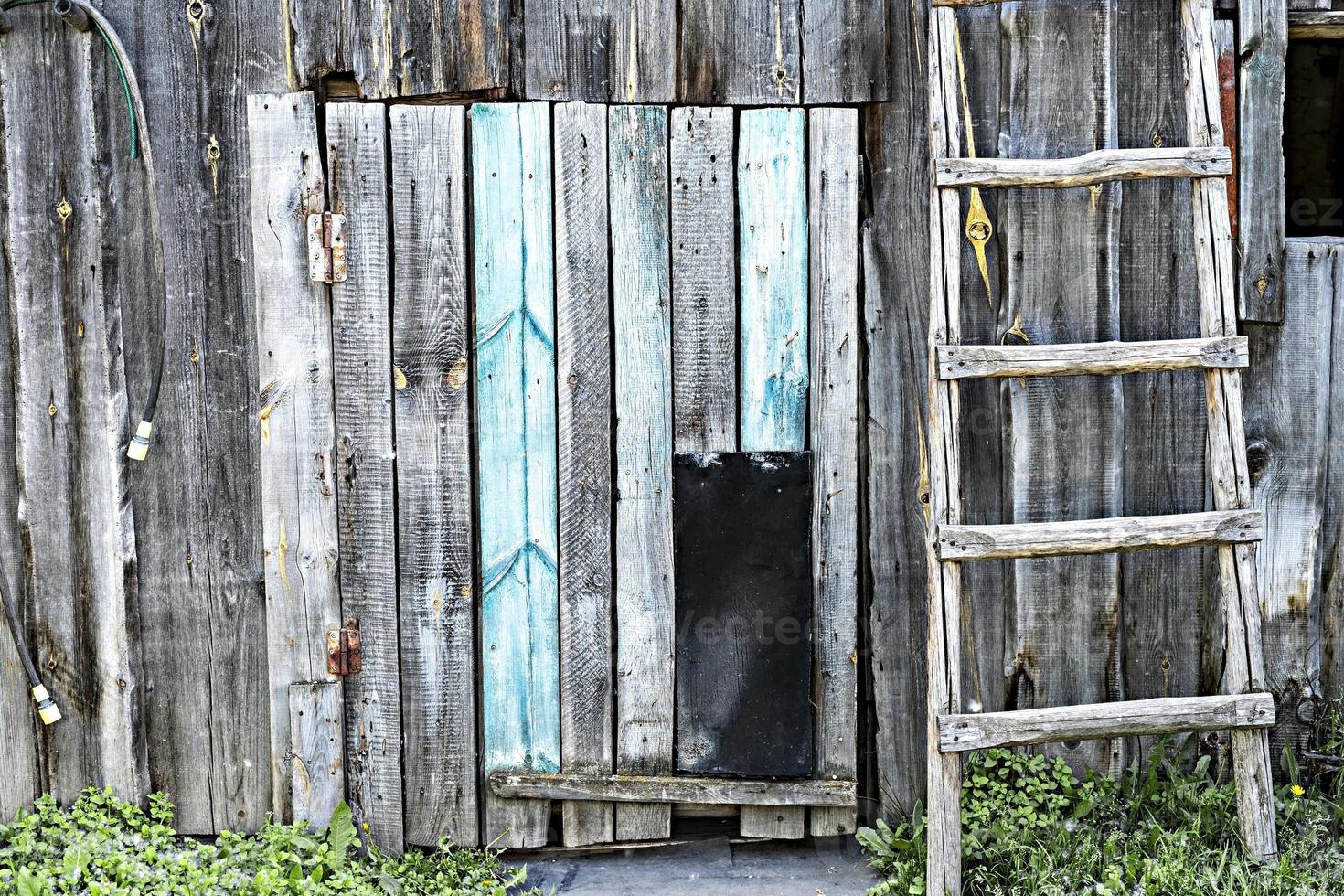 velha parede de prancha de madeira azul cinza rústica com porta de passagem para cães e escada de madeira foto