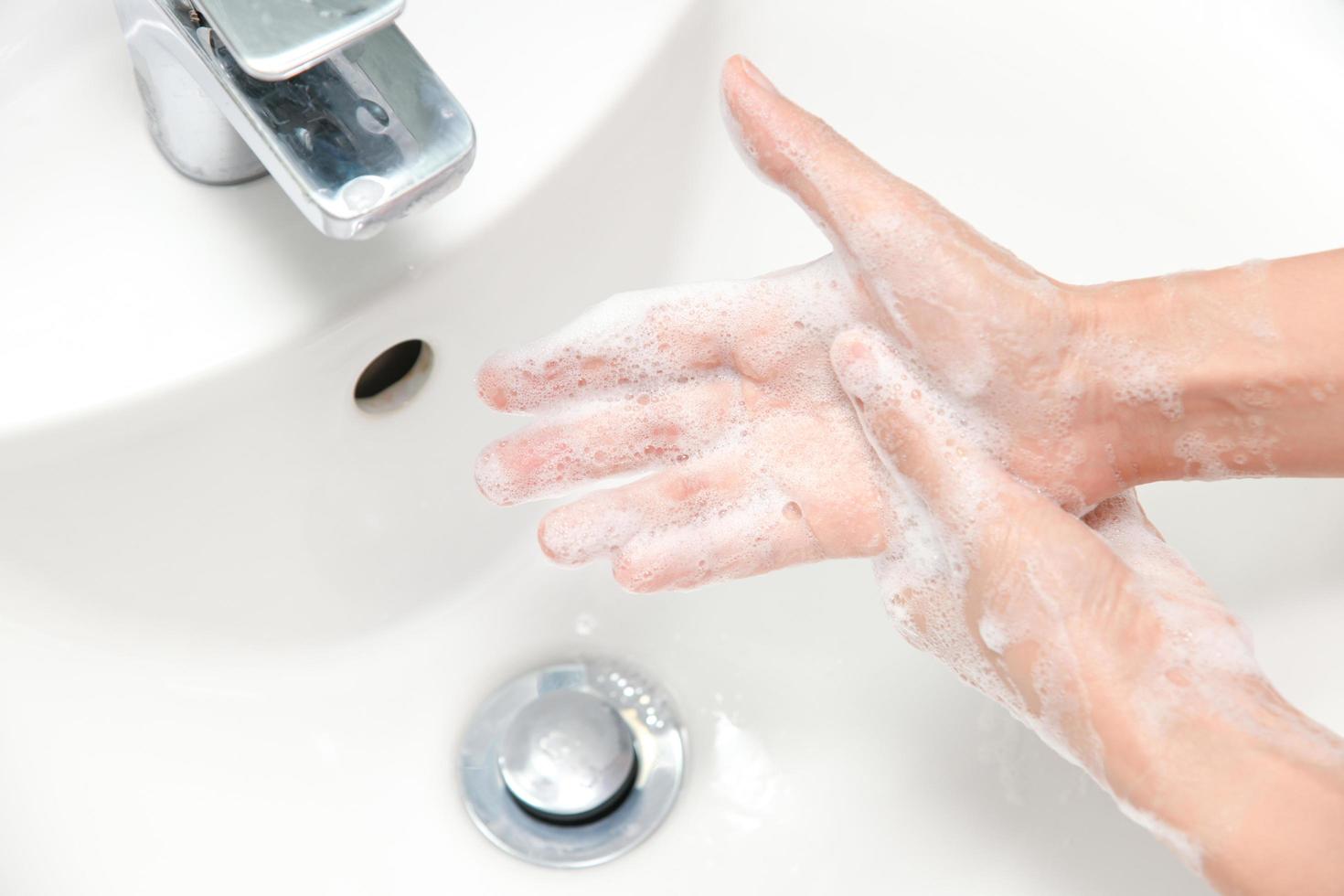 mulher usa sabão e lava as mãos sob a torneira de água. foto