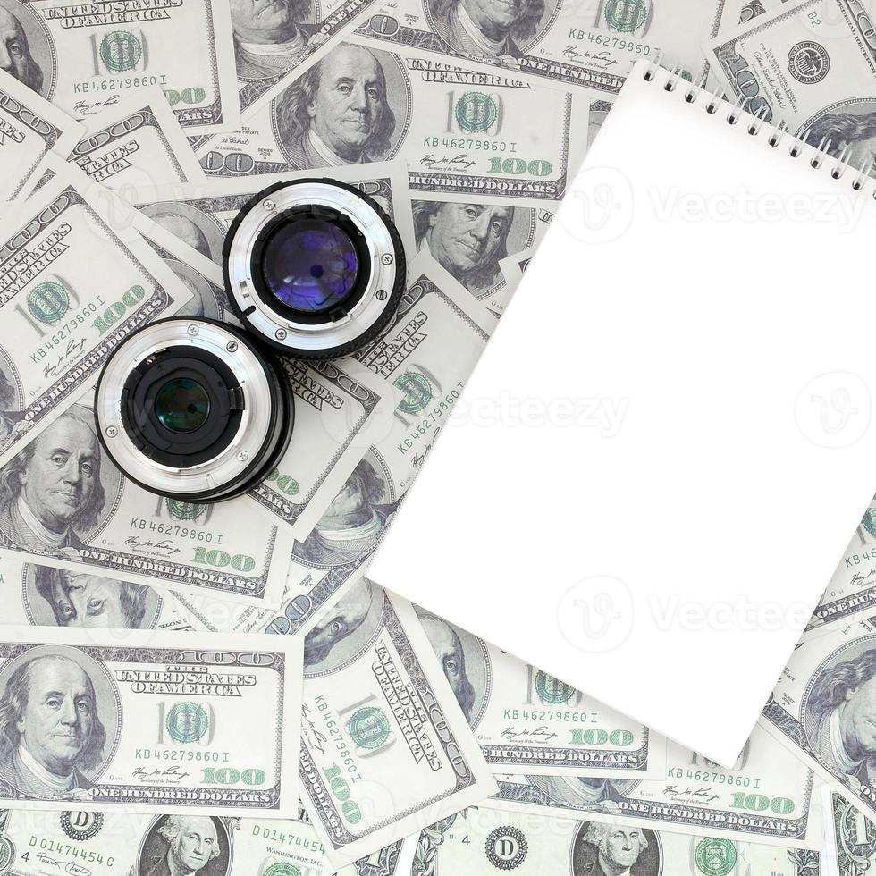 duas lentes fotográficas e um caderno branco estão no fundo de muitas notas de dólar. espaço para texto foto