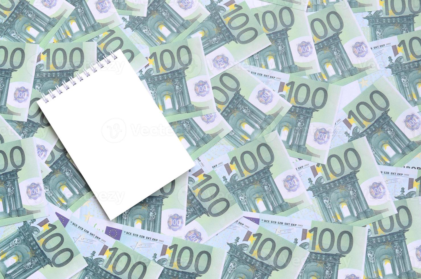 caderno branco com páginas limpas sobre um conjunto de denominações monetárias verdes de 100 euros. muito dinheiro forma uma pilha infinita foto