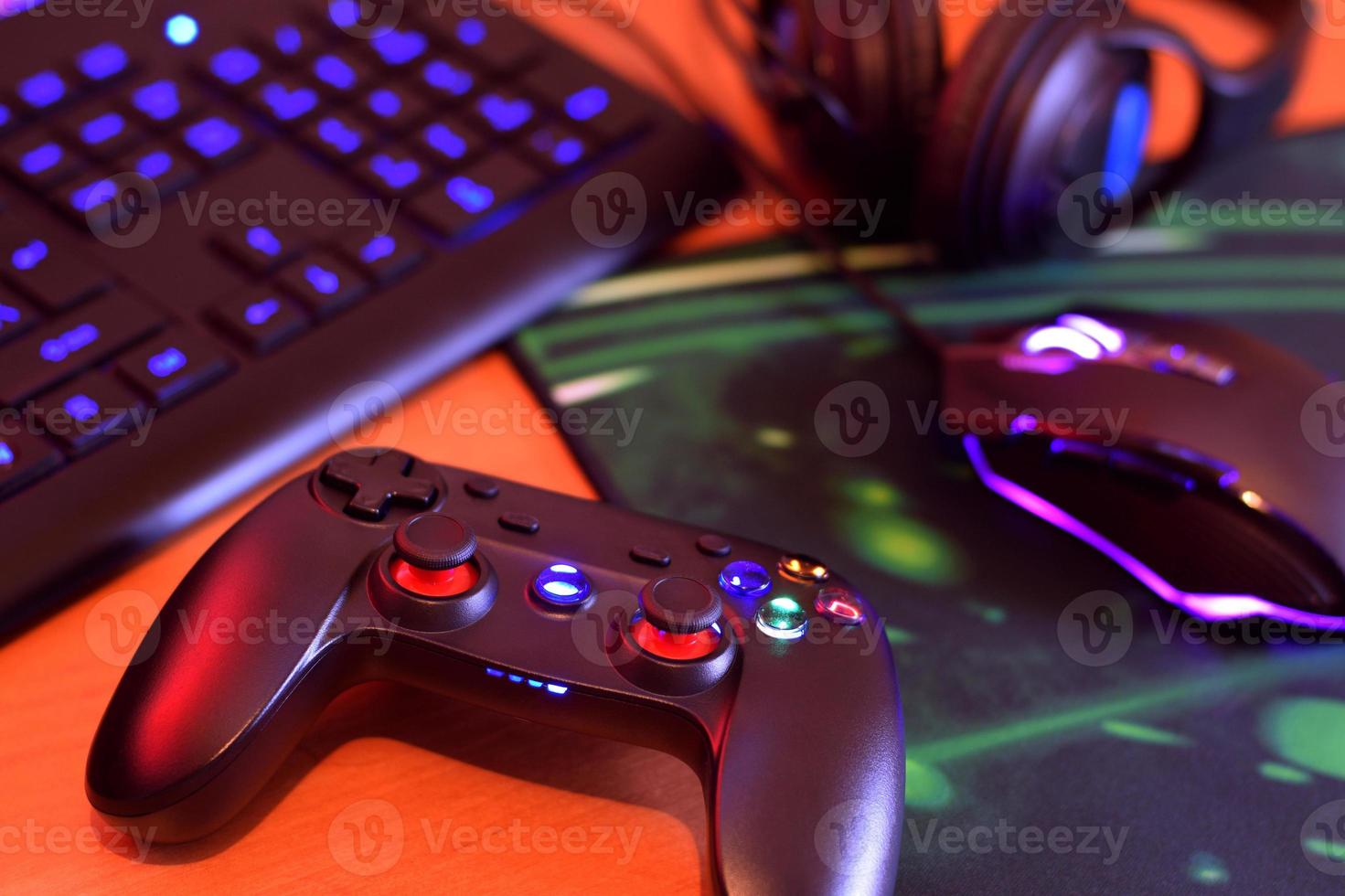 gamepad moderno e mouse para jogos encontra-se com teclado e fones de ouvido na mesa na cena da sala de jogos escura. conceito de desafios e competições de videogame foto