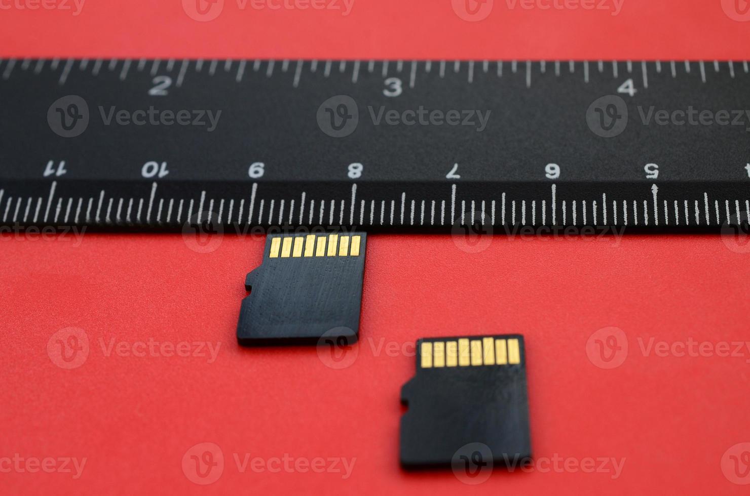 dois pequenos cartões de memória micro SD estão sobre um fundo vermelho ao lado de uma régua preta. um armazenamento de dados e informações pequeno e compacto foto