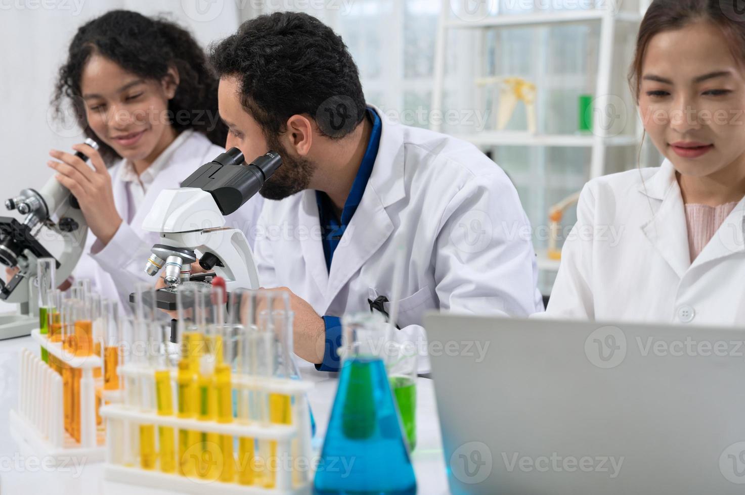 equipe de cientistas em jaleco branco trabalhando com microscópio e laptop para pesquisa em laboratório de pesquisa científica foto