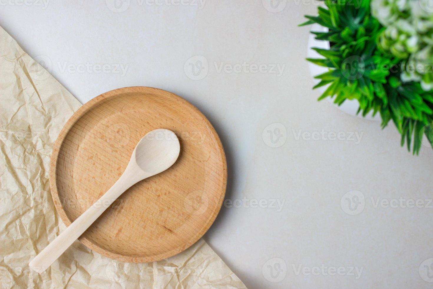 utensílios de madeira na mesa da cozinha. prato redondo, uma colher, uma planta verde. o conceito de servir, cozinhar, cozinhar, detalhes do interior. vista do topo foto