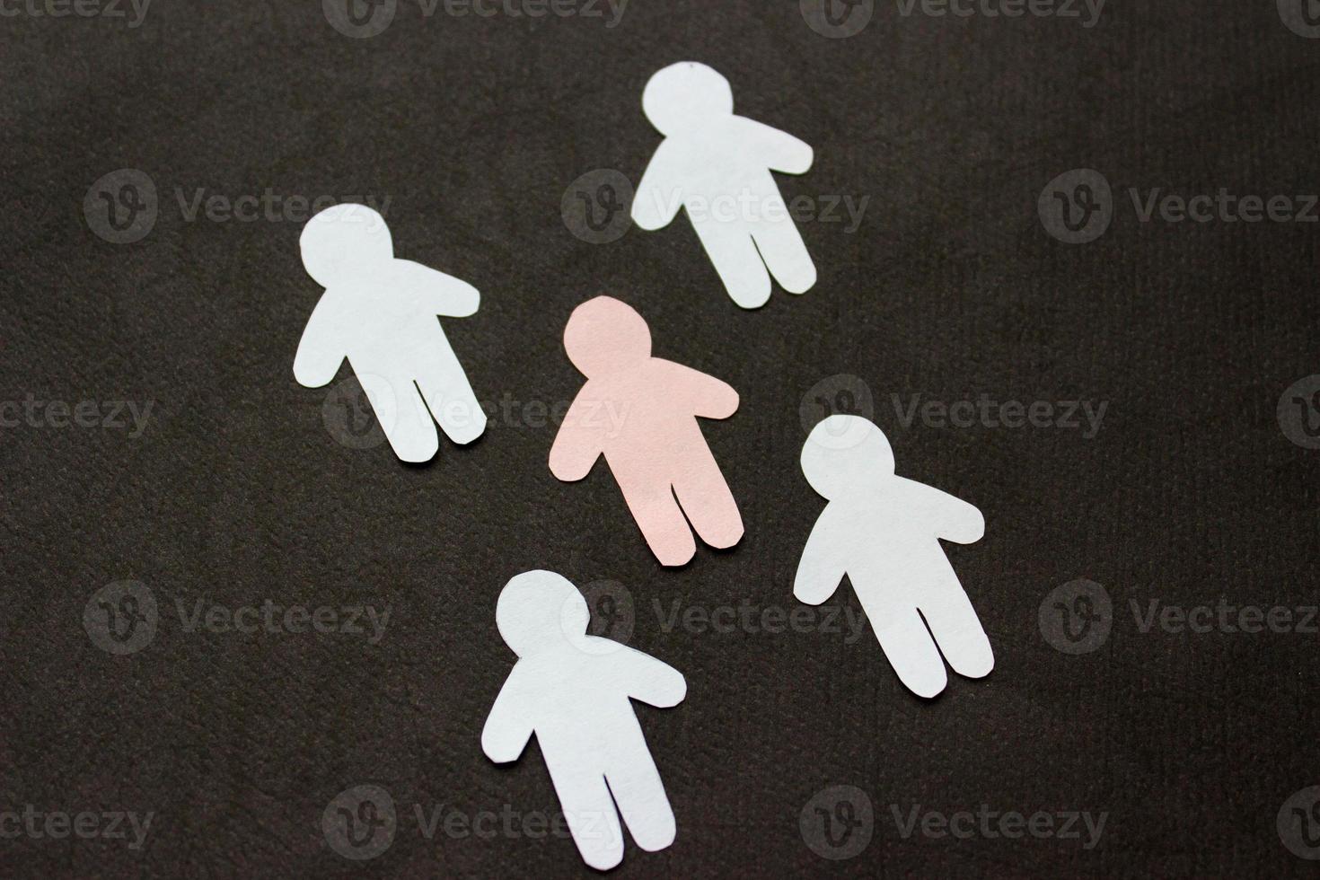 silhuetas de cinco homens, cortadas de papel. entre os homens brancos há um homem rosa. em fundo preto foto