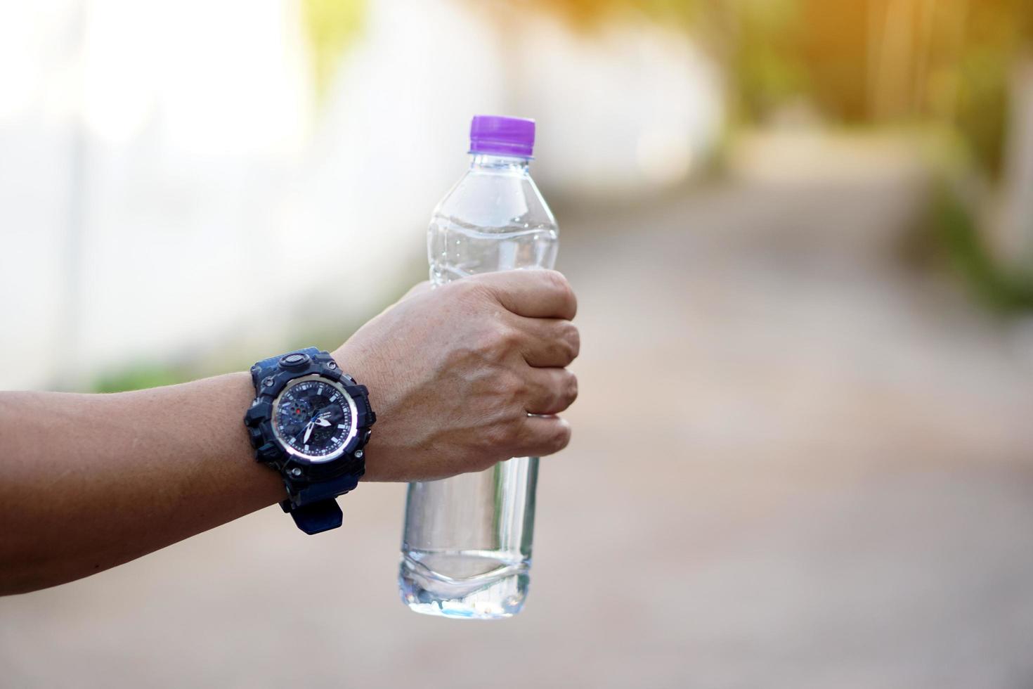 feche a mão segure a garrafa de água potável com tampa roxa. conceito beber água para a saúde, refrescar o corpo, aliviar a sede. foto