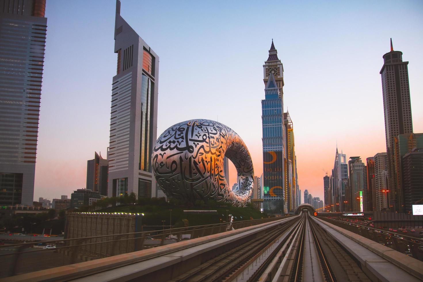 dubai, emirados árabes unidos, 2022 - trem de metrô na ferrovia em dubai com museu do futuro e fundo do céu pôr do sol foto