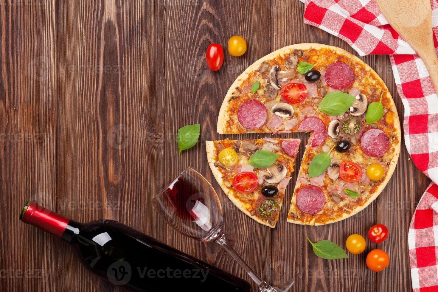 pizza italiana com calabresa, tomate, azeitonas, manjericão e wi vermelho foto