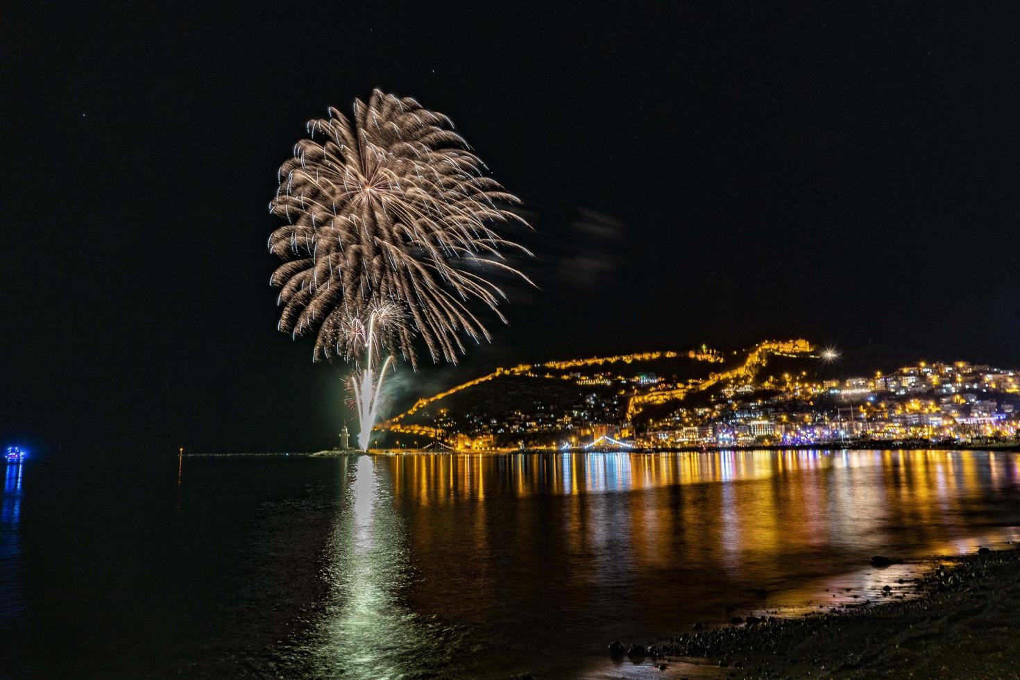 maravilhoso reflexo de fogos de artifício noturnos no mar e vista para o mar da cidade foto