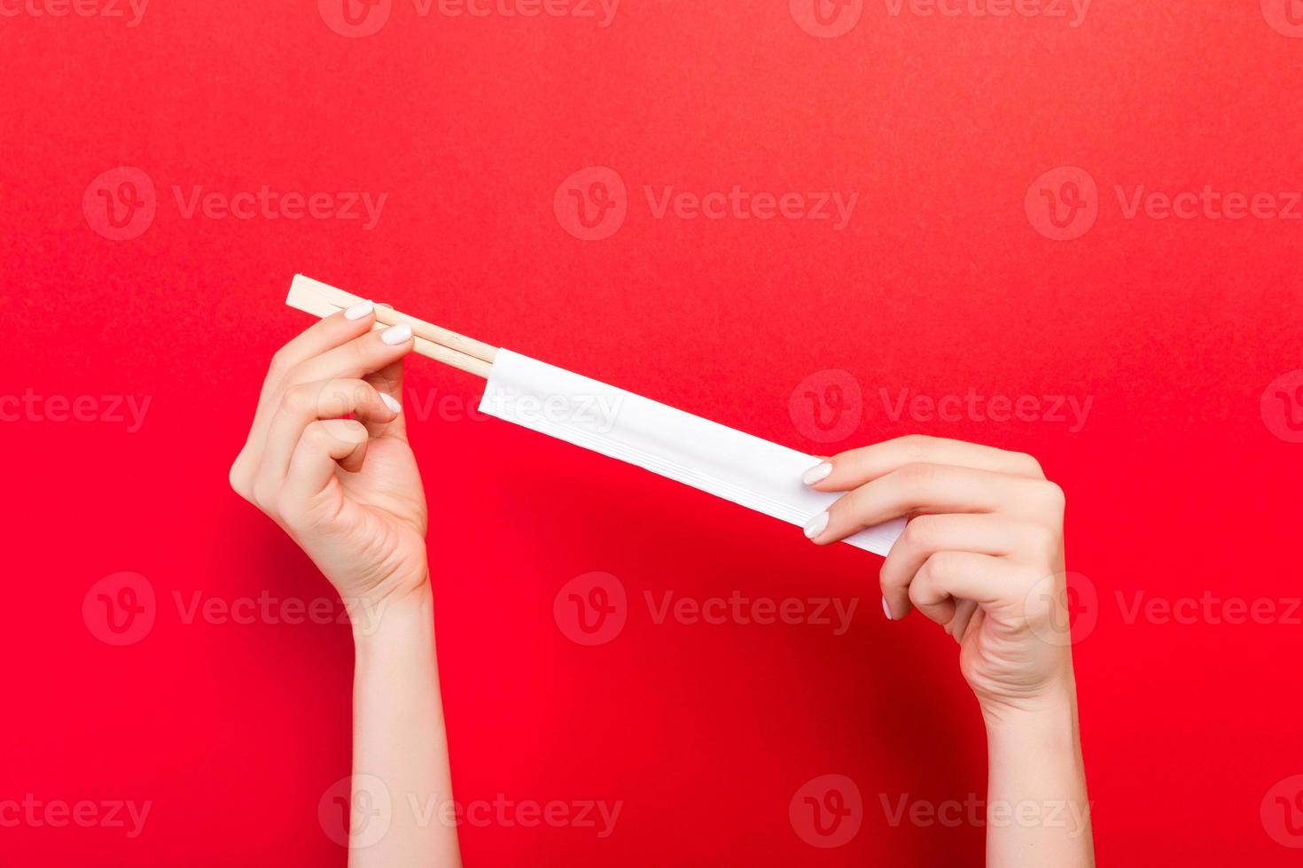 corte a imagem de duas mãos femininas segurando pauzinhos sobre fundo vermelho. pronto para comer o conceito com espaço de cópia foto