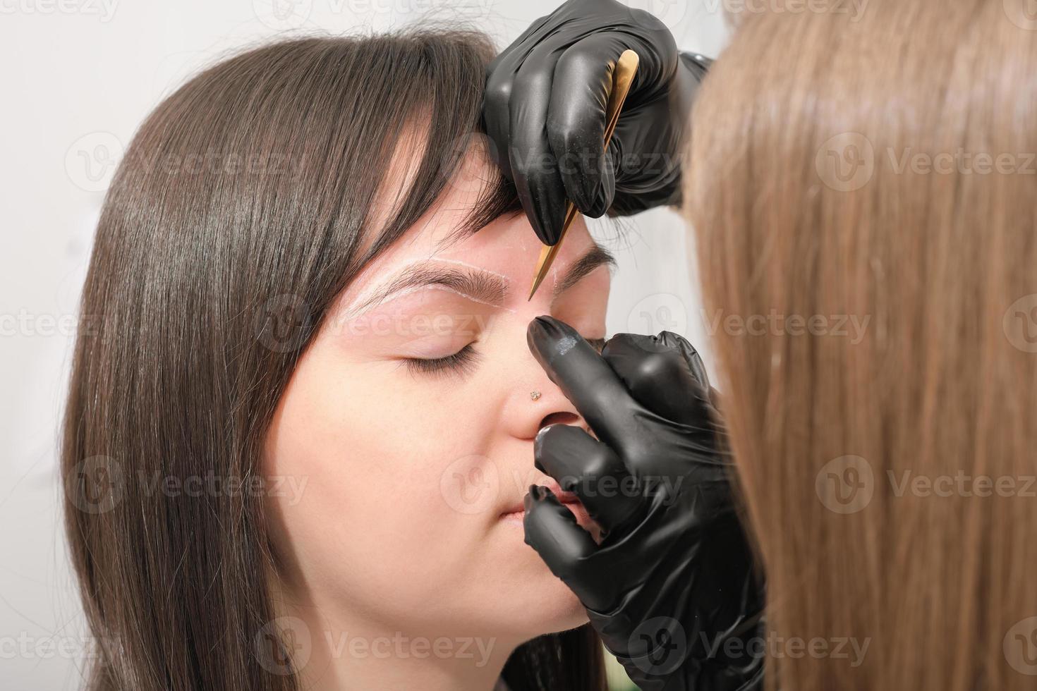 cosmetologista de sobrancelha de mulher fazendo marcas nas sobrancelhas do cliente com tinta branca. processo de mapeamento de sobrancelha. foto