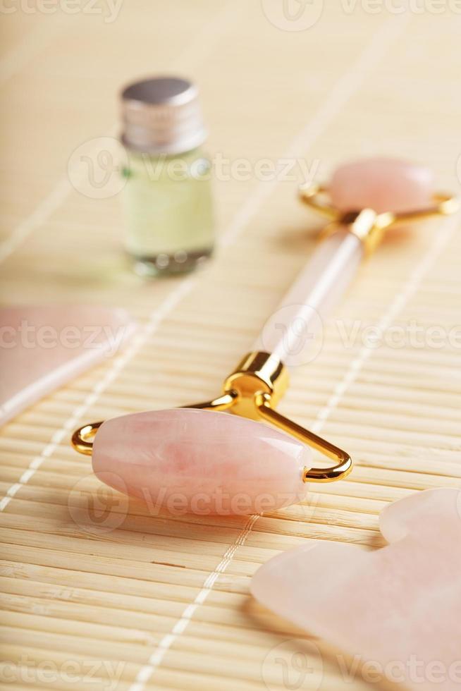 um conjunto de ferramentas para a técnica de massagem facial gua sha feita de quartzo rosa natural. rolo, pedra jade e óleo em uma jarra de vidro, em um fundo de palha para cuidados com o rosto e corpo. foto