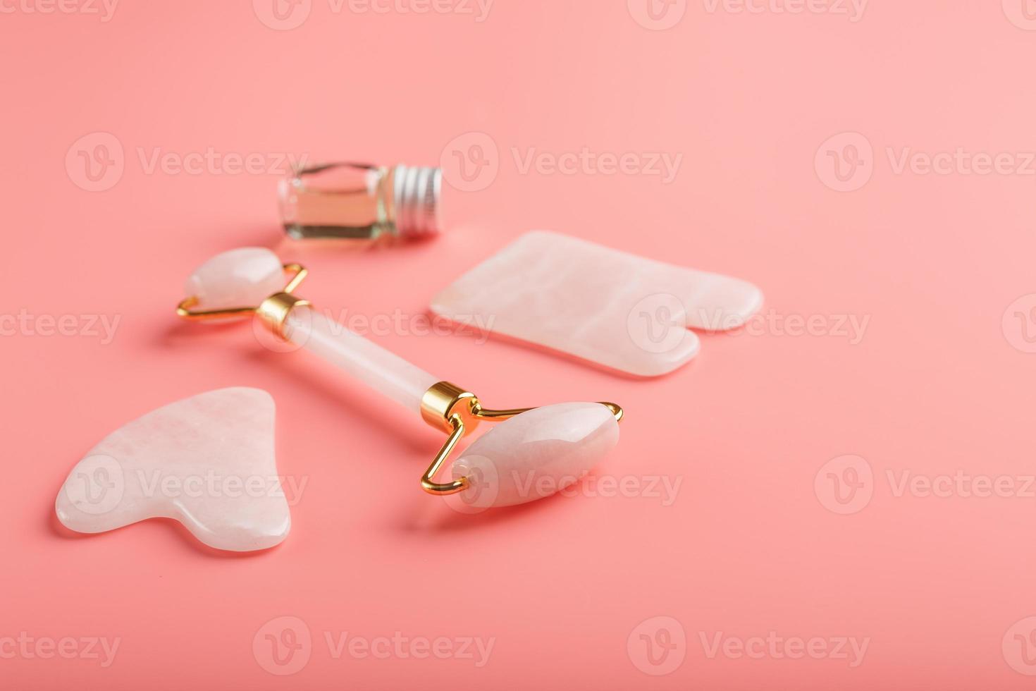 Ferramenta de massagem gua sha feita de rolo de quartzo rosa natural, pedra jade e óleo, em um fundo rosa para cuidados com o rosto e corpo. parte da medicina tradicional chinesa foto