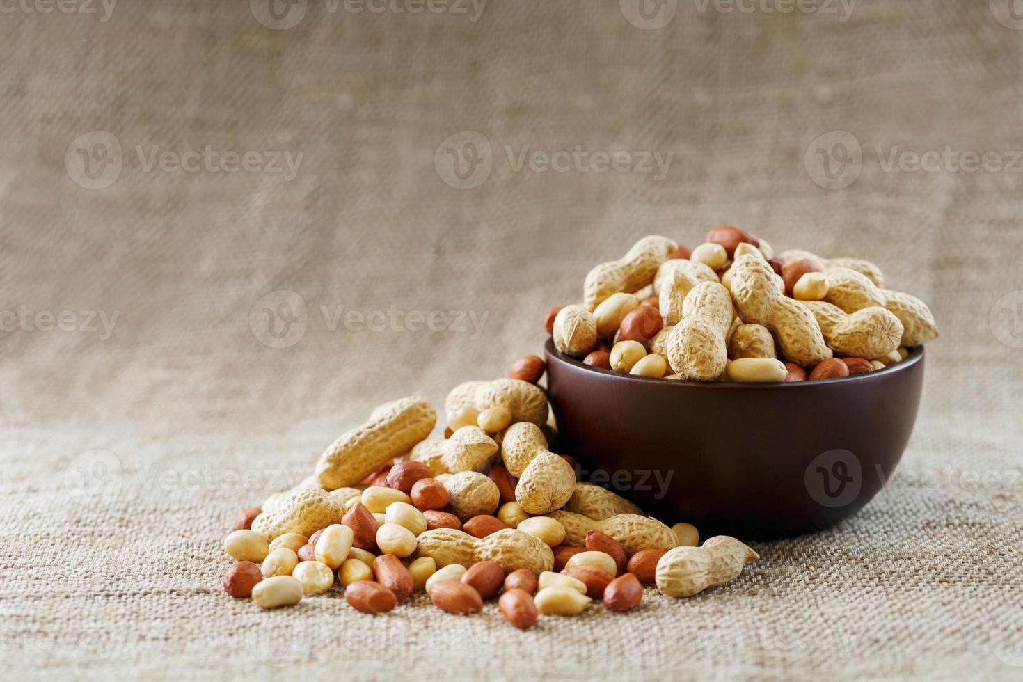 amendoins com casca e close-up descascado em xícaras. amendoins torrados com casca e descascados contra um pano marrom. foto