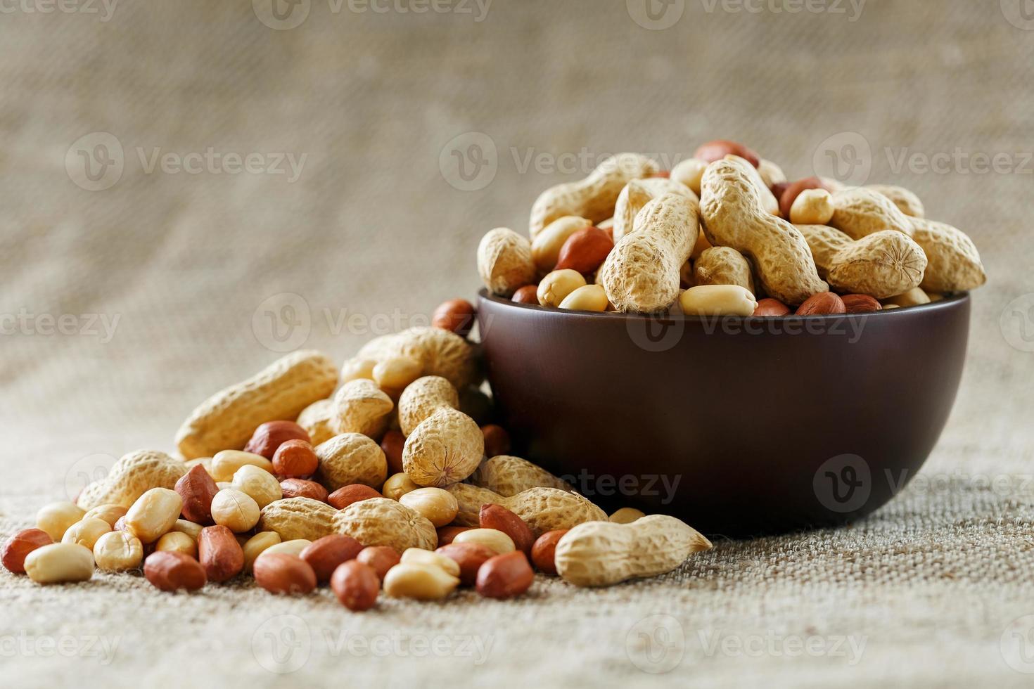 amendoins com casca e close-up descascado em xícaras. amendoins torrados com casca e descascados contra um pano marrom. foto
