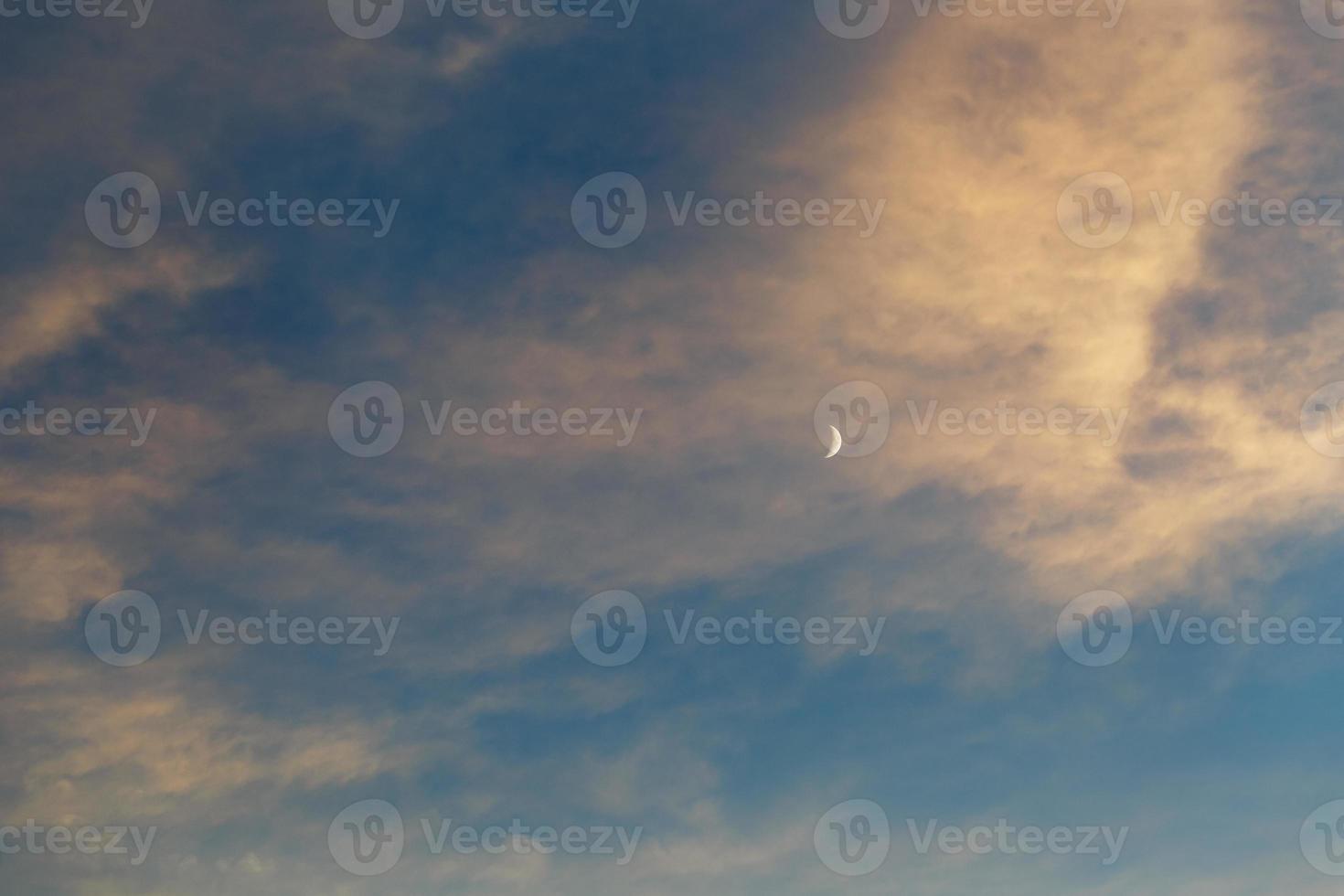 uma lua crescente no céu azul entre as nuvens iluminadas pelo sol ao pôr do sol foto