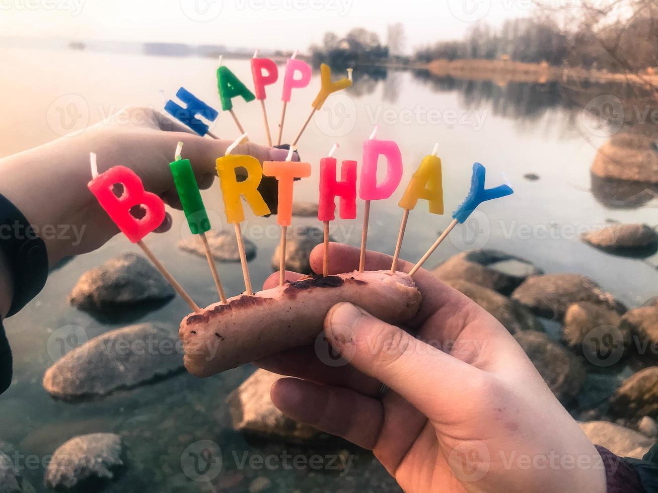 inscrição de feliz aniversário feita de velas de férias nas mãos de um homem e uma mulher em frente à água do rio lago oceano foto