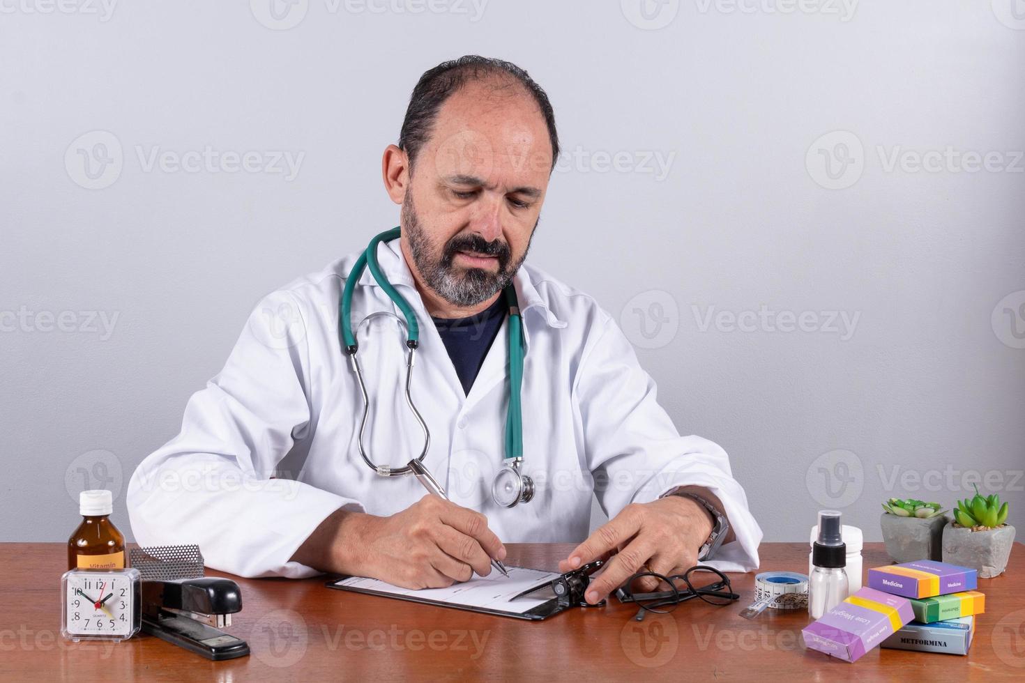 retrato de médico maduro sênior, agradável profissional de jaleco branco sentado à mesa foto
