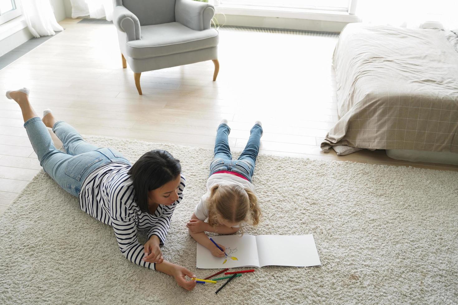 mãe desenhando com filha menina, deitada no chão em casa. hobby de arte, educação infantil foto