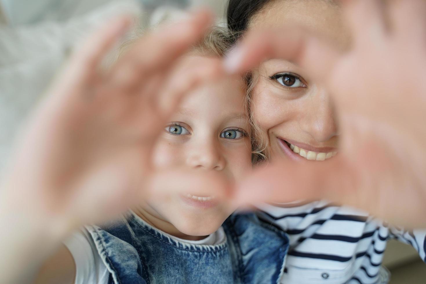 mãe adotiva sorridente, filha adotiva tomando selfie, mostrando gesto de coração de amor juntos foto
