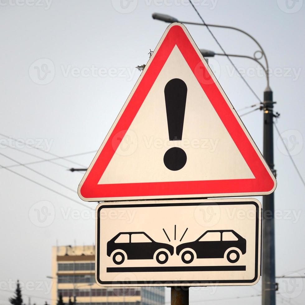 alto risco de colisão. um sinal de estrada com um ponto de exclamação e dois carros que colidiram um com o outro foto