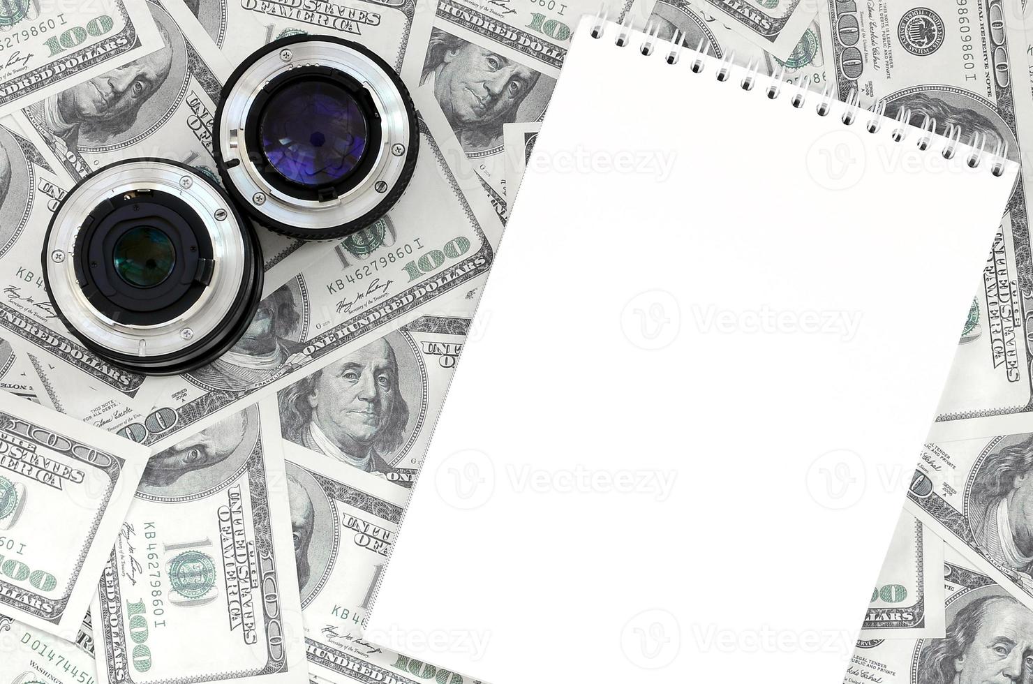 duas lentes fotográficas e um caderno branco estão no fundo de muitas notas de dólar. espaço para texto foto