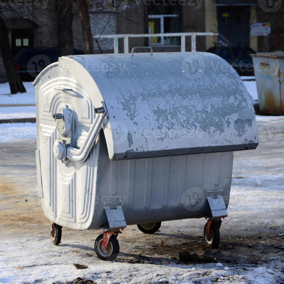 um recipiente de lixo prateado fica perto de edifícios residenciais no inverno foto