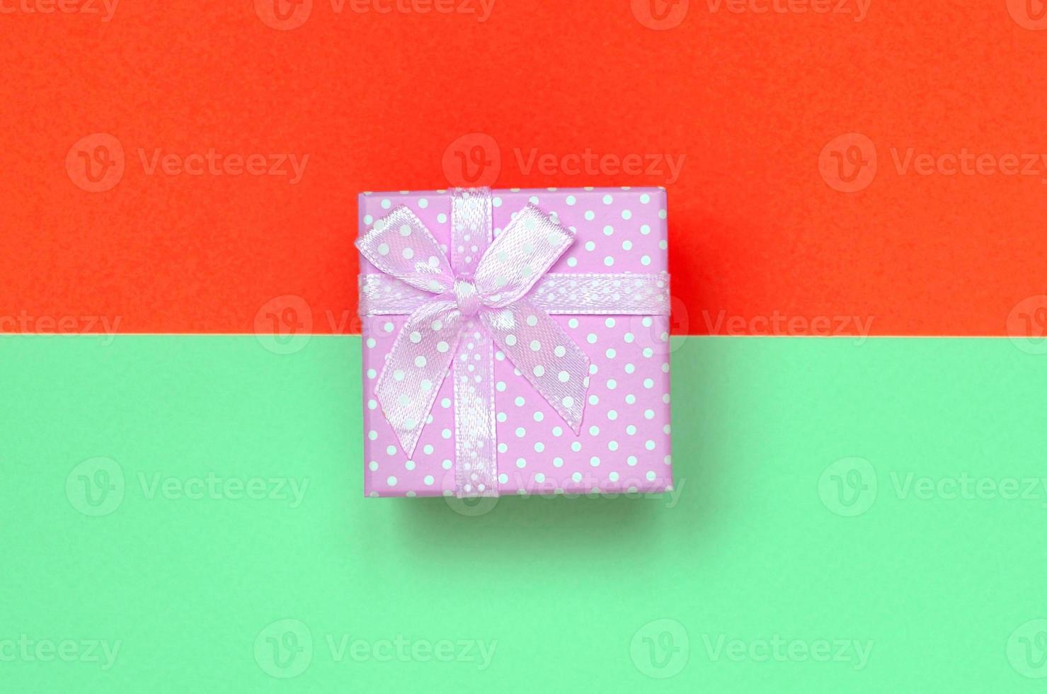 pequena caixa de presente rosa está no fundo de textura de papel de cores turquesa e vermelho pastel de moda foto